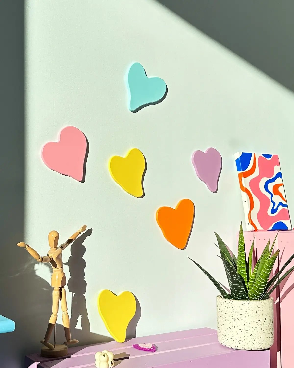 Les coeurs en pastel rose, bleu aqua, et jaune vibrant ajoutent une touche colorée et romantique à l'espace intérieur. Décoration murale moderne et minimaliste parfaite pour une chambre ou un salon.