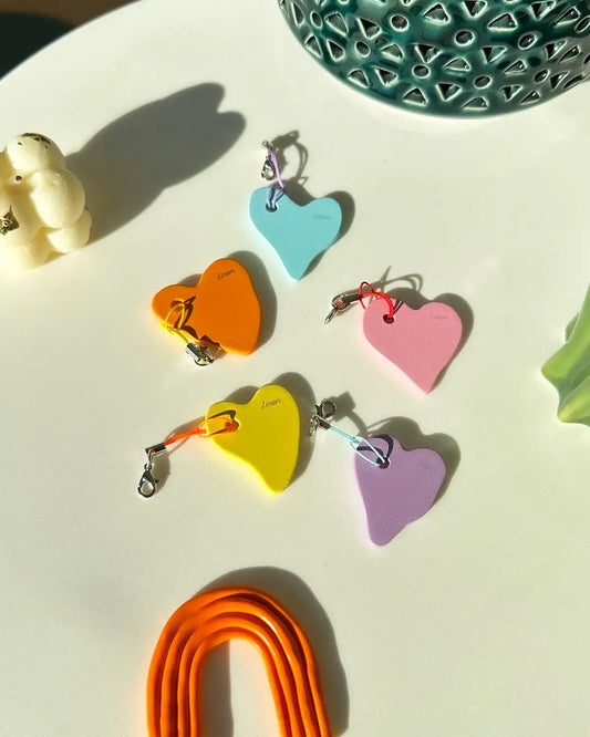 Porte-clés en forme de cœur en MDF aux couleurs vives disposés sur une table à côté d'une plante verte, idéaux pour un cadeau de couple ou pour exprimer l'amour 