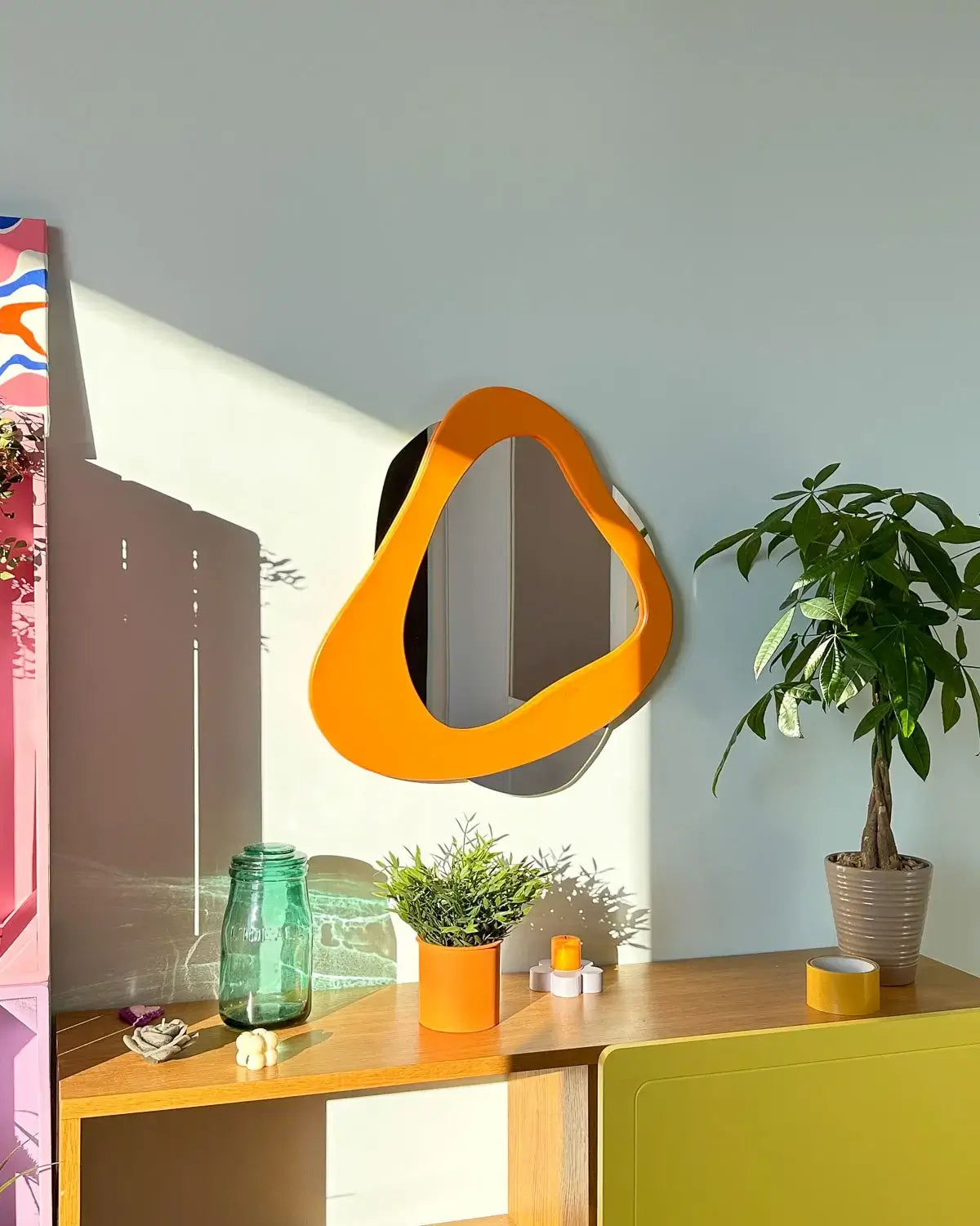 Miroir mural Sens de Vue de LinorHome, avec une forme organique asymétrique et un cadre orange vif, ajoutant une touche moderne et élégante à la pièce